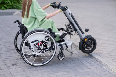 Tekerlekli sandalyedeki yüzü olmayan ve manuel kontrol için yardımcı bir aleti olan bir kadın. Elektrikli bisiklet.