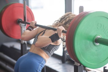 Orta yaşlı bir kadın spor salonunda halterle çömeliyor.