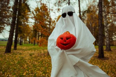 Beyaz çarşaflı kadın, sonbahar ormanlarında Jack Olantern 'ı tutuyor. Cadılar Bayramı kostümü