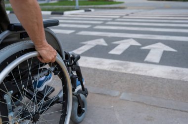 Tekerlekli sandalyedeki yaşlı bir kadının yaya geçidine gidişinin arka görüntüsü. Tekerlekler üzerinde yakın plan