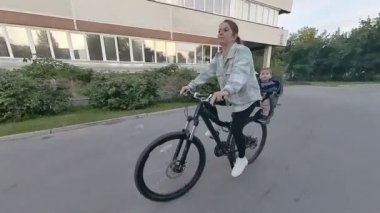 Beyaz kadın oğlunu bisiklet koltuğunda taşıyor.