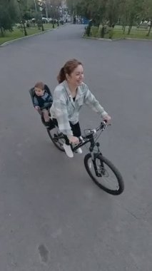 Beyaz kadın oğluyla bisiklete biniyor. Dikey video