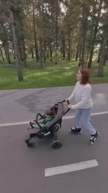 Beyaz kadın, yürümekte olan oğluyla bebek arabasında paten kayıyor. Dikey video