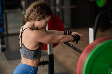 Spor salonunda halterde poz veren orta yaşlı bir kadın.