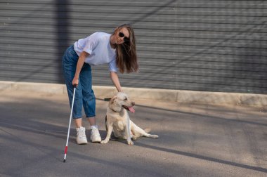 Kör bir kadın rehber köpeğini sokakta gezdirir. Labradora sarılan kız