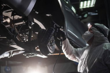 The master sprays an anti-corrosion compound on the bottom of the car clipart