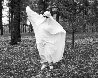 Bir sonbahar ormanının arka planında hayalet kostümlü bir kadın. Cadılar Bayramı kostümü. Siyah beyaz fotoğraf