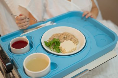 Beyaz kadın hastane yatağında yemek yiyor.