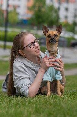 Küçük bir köpekle yürürken çimenlerde yatan beyaz bir kadın.