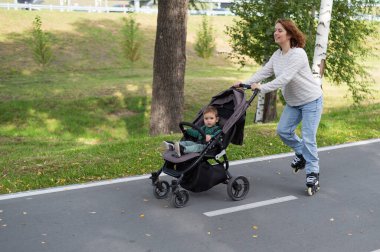 Beyaz kadın bebek arabasıyla küçük oğluyla paten kayıyor.