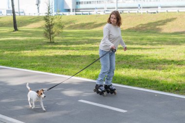 Beyaz kadın, Jack Russell Terrier köpeğiyle parkta paten kayıyor.