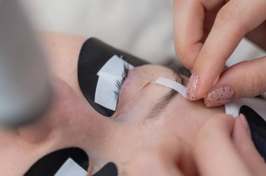 Bir uzman, kirpik uzatmadan önce göz kapaklarını indiren bir hastayı yapıştırır.