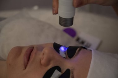 Kirpik uzatma prosedüründen geçen bir kadın ultraviyole lamba kullanıyor.