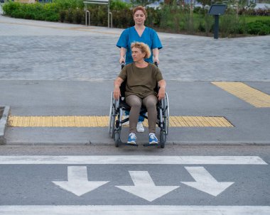 Kızıl saçlı hemşire yaşlı bir kadını yolun karşısına itiyor.