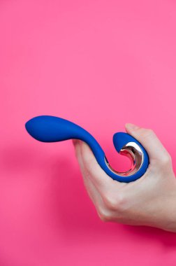 Pembe arka planda mavi vibratörlü bir el. Dikey fotoğraf