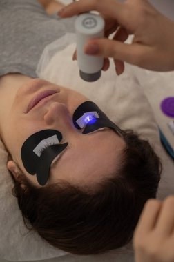 Kirpik uzatma prosedüründen geçen bir kadın ultraviyole lamba kullanıyor.