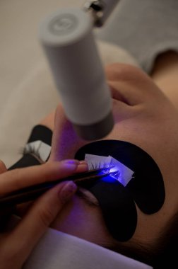 Kirpik uzatma prosedüründen geçen bir kadın ultraviyole lamba kullanıyor.