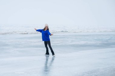 Caucasian woman in a blue sweater is skating on a frozen lake. The figure skater performs the program