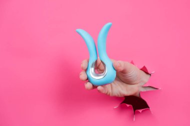 Pembe kağıttan yapılmış arka planda mavi kıvrımlı vibratör seks oyuncağı olan bir kadın eli.