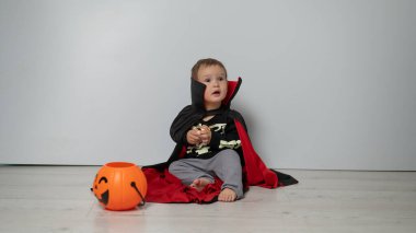 Beyaz arka planda kafatası tutan Drakula kostümlü küçük beyaz çocuk.