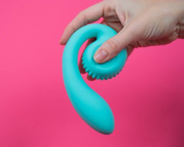 Pembe arka planda mavi eğimli seks oyuncağı tutan kadın.