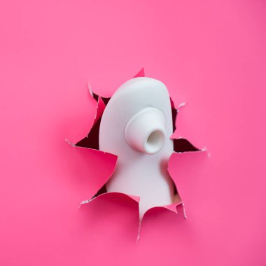 Beyaz vakumlu klitoral vibratör pembe kağıt arkaplanından sarkıyor. Seks oyuncağı