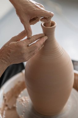 Çömlekçi, çömlekçi çarkında vazonun yüzeyini düzleştiren bir aletle çalışır. Bir erkeğin ellerine yakın çekim