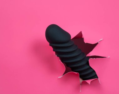 Black ribbed dildo sticking out of hole on pink background