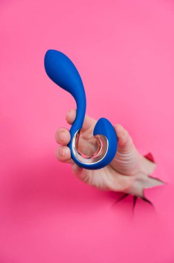 Pembe arka planda mavi vibratörlü bir el. Dikey fotoğraf