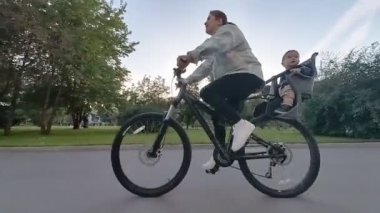 Beyaz kadın oğlunu bisiklet koltuğunda taşıyor.