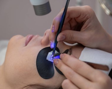 Kirpik uzatma prosedüründen geçen bir kadın ultraviyole lamba kullanıyor.