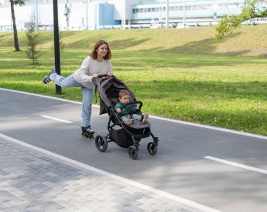 Beyaz kadın bebek arabasıyla küçük oğluyla paten kayıyor.