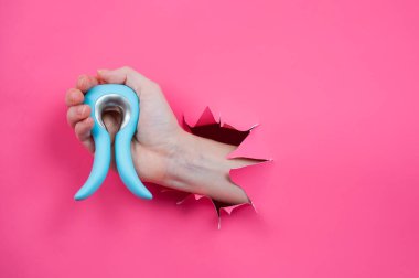 Pembe kağıttan yapılmış arka planda mavi vibratörlü seks oyuncağı olan bir kadın eli. Boşluğu kopyala