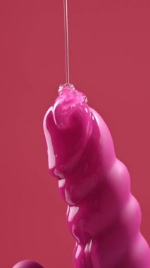 Lube pouring on black dildo on pink background. Vertical video