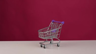 Adam beyaz süpürge klitoral seks oyuncağını pembe arka planda mini alışveriş arabasına koyuyor.