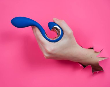 Mavi vibratörlü el pembe kağıt arkaplanından sarkıyor.