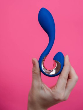 Pembe arka planda mavi kıvrımlı seks oyuncağı tutan kadın. Dikey fotoğraf