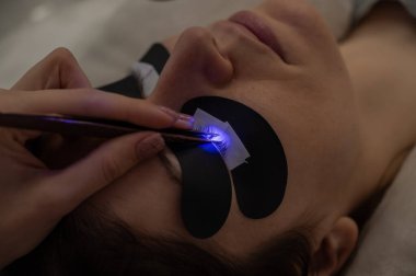 Kirpik uzatma prosedüründen geçen bir kadın ultraviyole lamba kullanıyor.