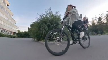 Beyaz kadın oğlunu bisiklet koltuğunda taşıyor.