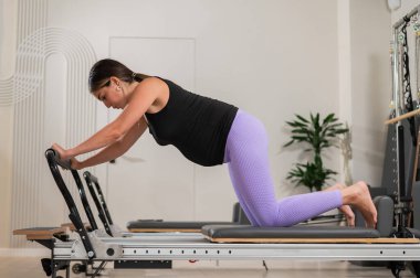 Hamile bir kadın yenilikçi bir makinede kalas kullanıyor. Perinatal yoga.