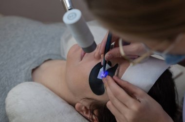 Kirpik uzatma prosedüründen geçen bir kadın ultraviyole lamba kullanıyor.