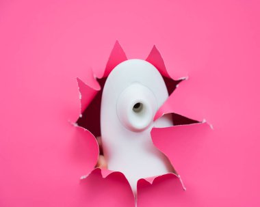 Beyaz vakumlu klitoral vibratör pembe kağıt arkaplanından sarkıyor. Seks oyuncağı