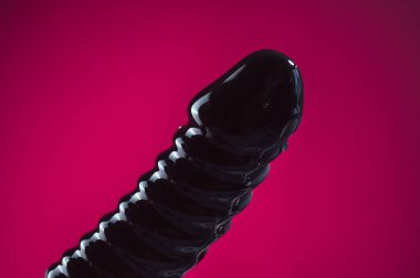 Lube pouring on black dildo on pink background