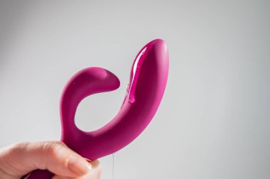 Lube pouring on pink dildo on white background