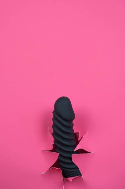 Black ribbed dildo sticking out of hole on pink background. Vertical video