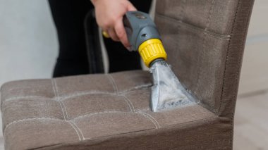 Kadın, elektrikli süpürgeyle kumaş sandalyesini temizliyor.