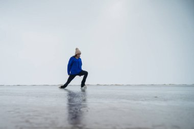 Mavi kazaklı beyaz kadın donmuş bir gölde paten kayıyor. Artistik patinajcı programı gerçekleştirir