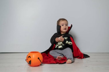 Beyaz arka planda kafatası tutan Drakula kostümlü küçük beyaz çocuk.