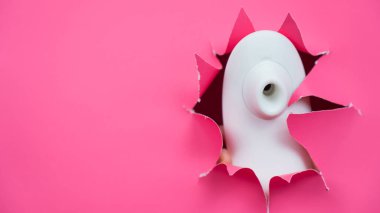 Beyaz vakumlu klitoral vibratör pembe kağıt arkaplanından sarkıyor. Seks oyuncağı