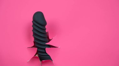 Black ribbed dildo sticking out of hole on pink background